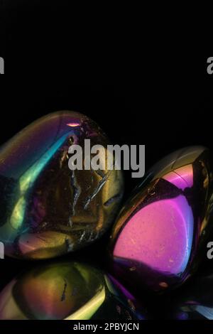 Closeup glänzend beschädigte Kieselsteine mit Regenbogenbeschichtung gegen schwarz bedeckt Hintergrund Stockfoto