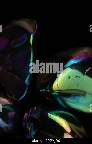 Closeup glänzend beschädigte Kieselsteine mit Regenbogenbeschichtung gegen schwarz bedeckt Hintergrund Stockfoto