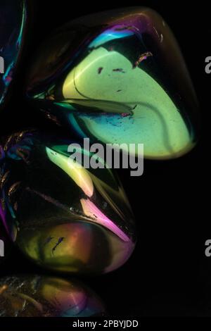 Closeup glänzend beschädigte Kieselsteine mit Regenbogenbeschichtung gegen schwarz bedeckt Hintergrund Stockfoto