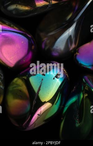 Closeup glänzend beschädigte Kieselsteine mit Regenbogenbeschichtung gegen schwarz bedeckt Hintergrund Stockfoto
