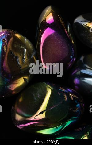 Closeup glänzend beschädigte Kieselsteine mit Regenbogenbeschichtung gegen schwarz bedeckt Hintergrund Stockfoto