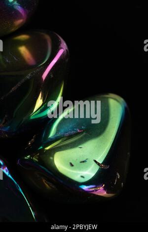 Closeup glänzend beschädigte Kieselsteine mit Regenbogenbeschichtung gegen schwarz bedeckt Hintergrund Stockfoto