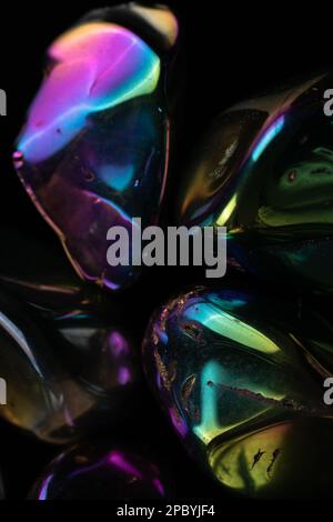 Closeup glänzend beschädigte Kieselsteine mit Regenbogenbeschichtung gegen schwarz bedeckt Hintergrund Stockfoto