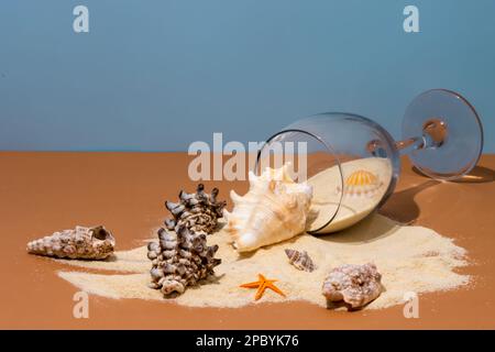 Von oben auf beigefarbenem Tisch mit verschüttetem Sand und verschiedenen Muscheln in der Nähe von Seesternen vor blauem Hintergrund Stockfoto