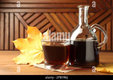 Flasche und ein Glas leckeren Ahornsirup auf einem Holztisch Stockfoto