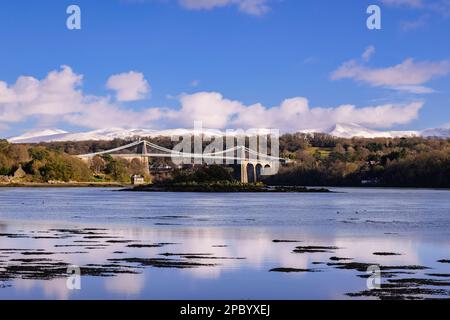 Blick aus dem niedrigen Winkel auf die Menai-Hängebrücke über die Menai-Straße mit Schnee auf den Bergen im Winter. Menai Bridge (Porthaethwy) Isle of Anglesey Wales UK Stockfoto