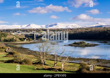 Malerischer Blick auf die Menai-Hängebrücke, die die Menai-Straße überquert, mit Schnee auf den Bergen im Winter. Menai Bridge (Porthaethwy), Isle of Anglesey, Wales, Vereinigtes Königreich Stockfoto