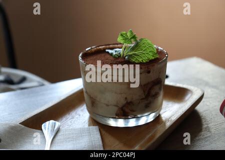 Ein köstliches Tiramisu-Dessert im Glas auf einem rustikalen Holztablett auf einem Tisch Stockfoto