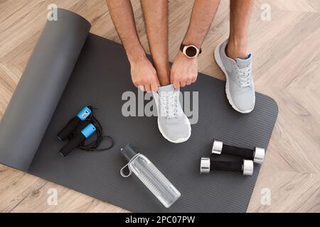 Draufsicht auf den Mann, der Turnschuhe, Yoga-Matte, Flasche, Seil und Kurzhanteln anzieht Stockfoto