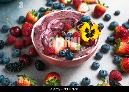 Zwei Sommer-acai-Smoothie-Schalen mit Erdbeeren, Blaubeeren, auf grauem Betonhintergrund. Frühstücksschale mit Obst und Müsli, Nahaufnahme, Draufsicht Stockfoto