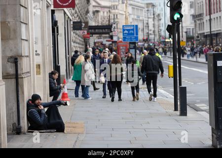 Ein Obdachloser sitzt in Piccadilly und hofft auf Spenden, während er mit einem Schild aus Pappe in London, England, Großbritannien für seine Hungersnot wirbt Stockfoto