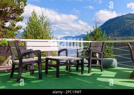 Sommerterrasse mit Gartenmöbeln an einem sonnigen Tag, leere Tische und Stühle an der Seeküste Stockfoto