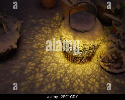 Die solarbetriebene Gartenlaterne im britischen Winter wirft ein wunderschönes Licht- und Schattenmuster über einen schneebedeckten Tisch Stockfoto