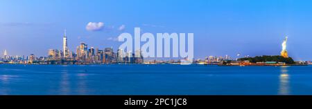Die Skyline von New York, New York und den USA vom Hafen mit Ellis Island und der Freiheitsstatue in der Abenddämmerung. Stockfoto
