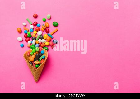 Waffelkonus voller traditioneller Süßigkeiten, die auf farbigen Hintergrund fallen, mit Platz für Kopien. Frohes Weihnachtsangebot. Stockfoto