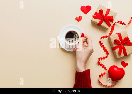 Flache Lage einer herzförmigen Tasse schwarzen Kaffees in den Händen von Frauen auf farbigem Hintergrund mit Kopierbereich Draufsicht. Valentinstag- und Feiertagskonzept. Stockfoto