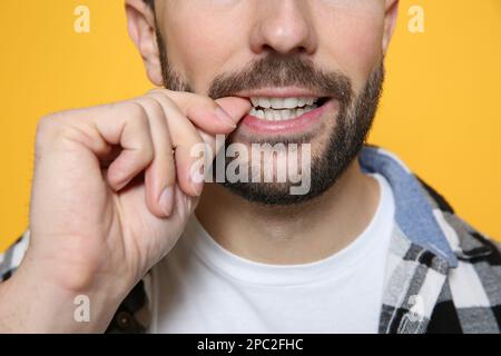 Ein Mann, der sich auf gelbem Hintergrund an den Nägeln biss, Nahaufnahme Stockfoto