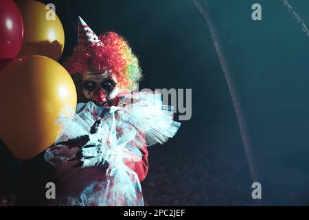 Furchteinflößender Clown mit Luftballons draußen in der Nacht. Halloween-Party-Kostüm Stockfoto