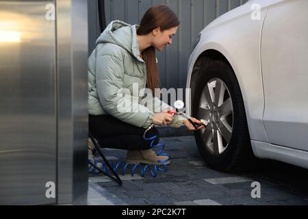 Junge Frau, die beim Autoservice Reifen aufpumpt Stockfoto