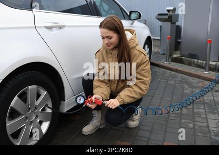 Junge Frau, die beim Autoservice Reifen aufpumpt Stockfoto