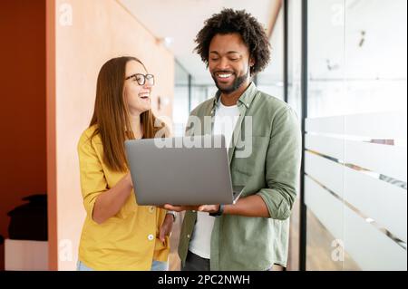 Büromitarbeiter treffen sich, sehen sich vor dem Laptop an und diskutieren. Zwei Kollegen diskutieren während der Kaffeepause, Kollegen führen ein freundliches Gespräch. Teamwork-Konzept Stockfoto