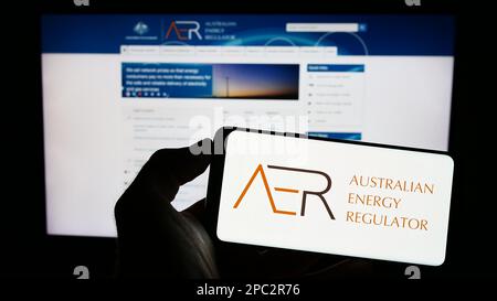 Person, die ein Mobiltelefon mit dem Logo der australischen Energieregulierungsbehörde (AER) auf dem Bildschirm vor der Webseite hält. Konzentrieren Sie sich auf das Display des Telefons. Stockfoto