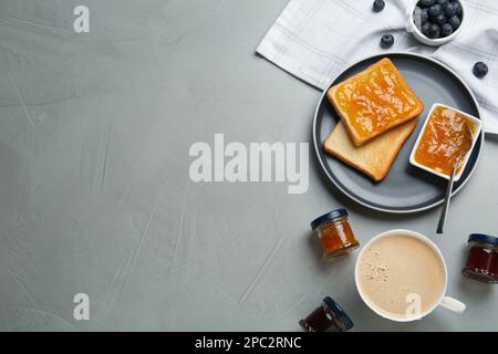 Toasts, verschiedene Marmeladen und eine Tasse Kaffee, serviert auf einem grauen Tisch, flach liegend. Platz für Text Stockfoto