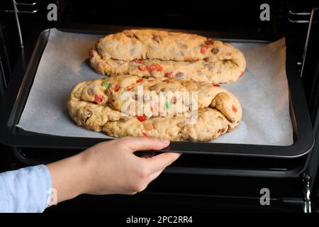 Eine Frau, die ein Backblech mit rohem, hausgemachtem Stollens in den Ofen legt, Nahaufnahme. Traditionelles deutsches Weihnachtsbrot Stockfoto