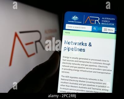 Person, die ein Mobiltelefon mit einer Webseite der australischen Energieregulierungsbehörde (AER) auf dem Bildschirm vor dem Logo hält. Konzentrieren Sie sich auf die Mitte des Telefondisplays. Stockfoto