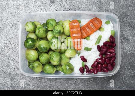 Schmackhafter Reis mit Schnitzeln und Gemüse in Kunststoffbehälter auf grauem Tisch, Draufsicht Stockfoto