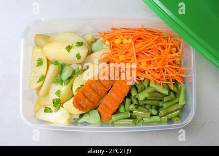 Leckere Kartoffeln mit Schnitzeln und Gemüse in einem Kunststoffbehälter auf einem leichten Tisch, Draufsicht Stockfoto