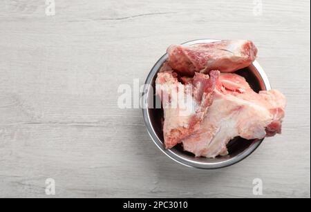 Fütterschüssel mit rohen Fleischknochen auf weißem Holztisch, Draufsicht. Platz für Text Stockfoto