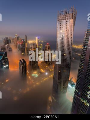 Aufnahmen bei Sonnenaufgang von der Dubai Marina bedeckt mit einer dicken Nebelschicht mit ihren futuristischen Wolkenkratzern, die zwischen den Nebel ragen. Aufgenommen in Dubai, VAE Stockfoto