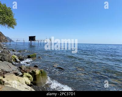 Verlassene hölzerne Pfahltürme Fischerhöhle am heimwerkerpier an der felsigen Küste des Fischerdorfes an sonnigen Sommertagen hellblauer Himmel Stockfoto