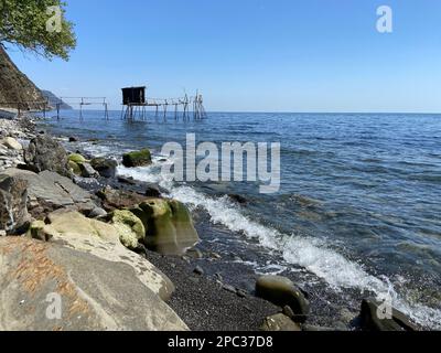 Verlassene hölzerne Pfahltürme Fischerhöhle am heimwerkerpier an der felsigen Küste des Fischerdorfes an sonnigen Sommertagen hellblauer Himmel Stockfoto