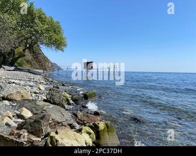 Verlassene hölzerne Pfahltürme Fischerhöhle am heimwerkerpier an der felsigen Küste des Fischerdorfes an sonnigen Sommertagen hellblauer Himmel Stockfoto