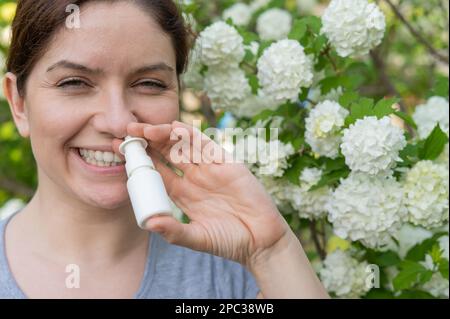 Kaukasische Frau verwendet ein Nasenspray, während sie im Park spazieren geht. Stockfoto