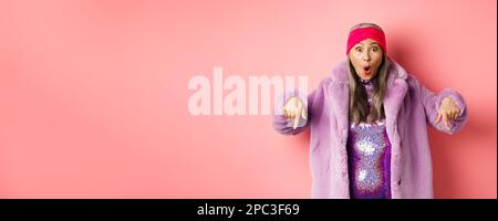 Mode- und Shopping-Konzept. Beeindruckt asiatische weibliche Zeigefinger nach unten und Blick aufgeregt bei der Kamera, zeigt genial promo Angebot, stehen über Stockfoto