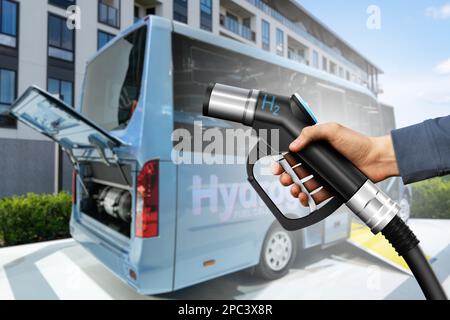 Hand mit Wasserstoffdüse und Bus mit offener Haube und H2-ml-Zylinder im Inneren. Sauberes Mobilitätskonzept Stockfoto