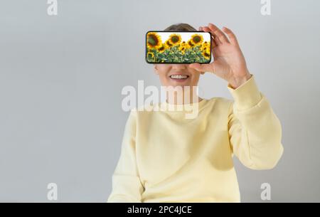 Eine Frau hält ein Smartphone mit Sonnenblumen auf dem Bildschirm in der Hand. Stockfoto