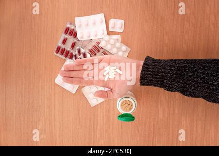 Draufsicht der Ernteguthände eines nicht erkennbaren Mannes, der Pillen in der Hand über verschiedenen Blasen von Medizin auf einem Holztisch zeigt Stockfoto