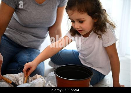 Menschen-, Garten- und Hausarbeit-Konzept - kleines Mädchen mit Gartenschaufel, schwarzer Erde in Plastiktopf Stockfoto