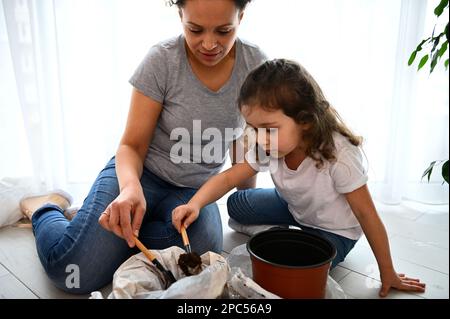 Mutter und Kind mit einer Gartenschaufel, befruchtete schwarze Erde in einen Plastiktopf geben, Setzlinge auf der Veranda Pflanzen Stockfoto