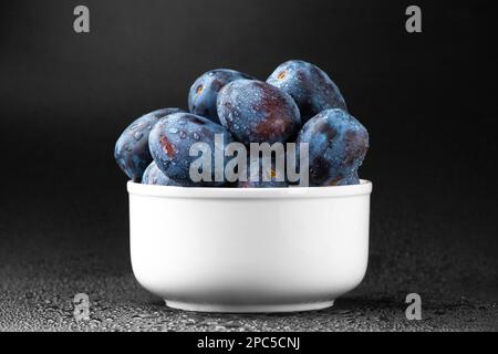 Blaue Pflaume auf einer weißen Platte mit Wassertropfen auf dunklem Hintergrund. Nützliche diätetische Früchte. Stockfoto
