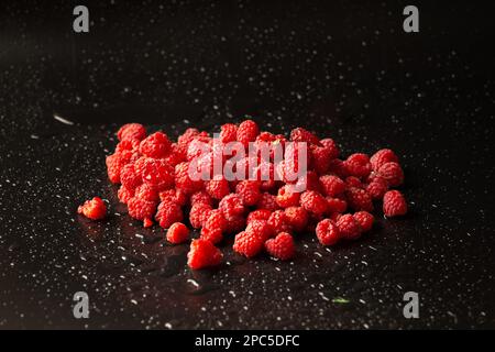 Ein Hügel roter Himbeeren mit Wassertropfen auf dunklem Hintergrund, Nahaufnahme. Nützliches Diätprodukt. Stockfoto