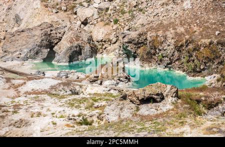 Türkisblaue Heißquellenwasser-Pfützen zwischen rissigen hellen Felsen und trockenem Buschwerk in einer Nahaufnahme am Hot Creek, Inyo National Forest, Kalifornien. Stockfoto