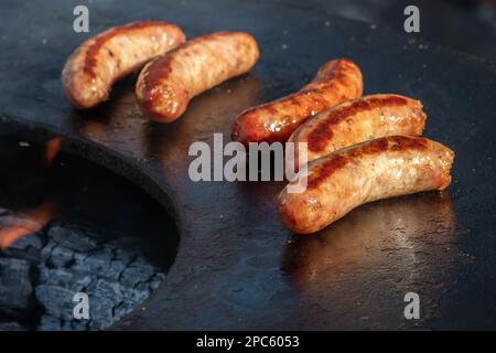 Schweinewürste, grillt oder geröstet in einem Barbecue an einem offenen Feuer, in einem Straßenmarkt oder einem Picknick im Freien, aus nächster Nähe Stockfoto
