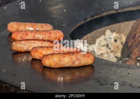 Schweinewürste, grillt oder geröstet in einem Barbecue an einem offenen Feuer, in einem Straßenmarkt oder einem Picknick im Freien, aus nächster Nähe Stockfoto