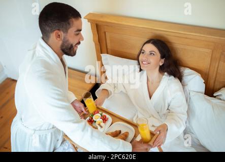 Glückliches Paar Beim Frühstück Im Bett, Das Im Hotelschlafzimmer Sitzt Stockfoto