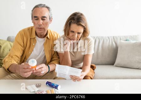 Besorgte pensionierte Großeltern, die sich Medikamente, Pillen, Tabletten in Blasen ansehen, am Tisch sitzen Stockfoto